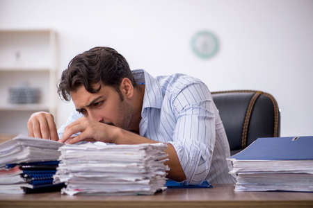 Young male employee and too much work in the officeの写真素材