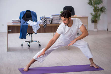 Young male employee doing sport exercises in the officeの写真素材