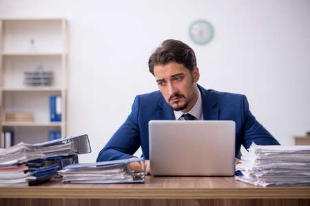 Young male employee and too much work in the officeの写真素材