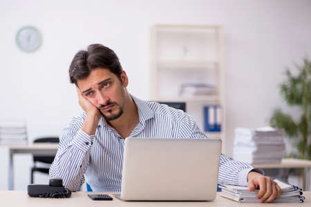 Young male employee and too much work in the officeの写真素材