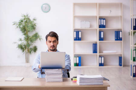 Young male employee and too much work in the officeの写真素材