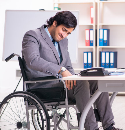 Young handsome employee in wheelchair at the officeの写真素材