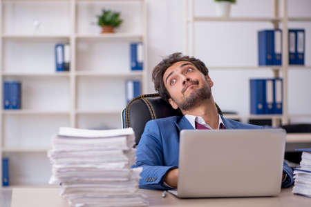 Young male employee and too much work in the officeの写真素材