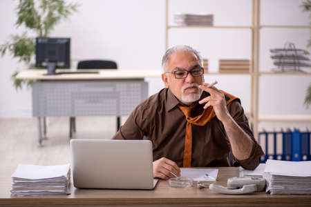 Old male employee smoking cigarette at workplaceの写真素材