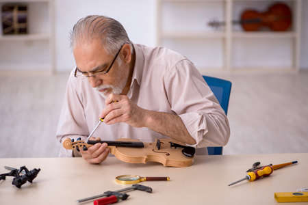 Old male repairman repairing musical instruments at workshopの写真素材