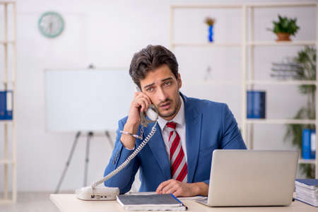 Handcuffed young male employee sitting in the officeの写真素材