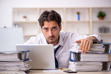 Young male employee and too much work in the officeの写真素材