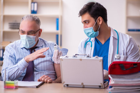 Young male doctor visiting old businessman at workplaceの写真素材