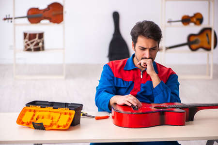 Young male repairman repairing musical instruments at workplaceの写真素材
