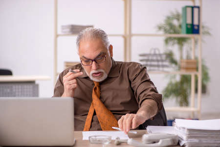 Old male employee smoking cigarette at workplaceの写真素材