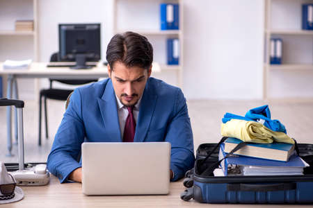 Young male employee preparing for trip at workplaceの写真素材