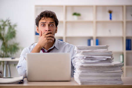Young male employee and too much work in the officeの写真素材