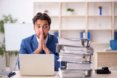 Young male employee and too much work in the officeの写真素材