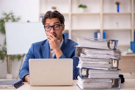 Young male employee and too much work in the officeの写真素材