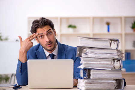 Young male employee and too much work in the officeの写真素材