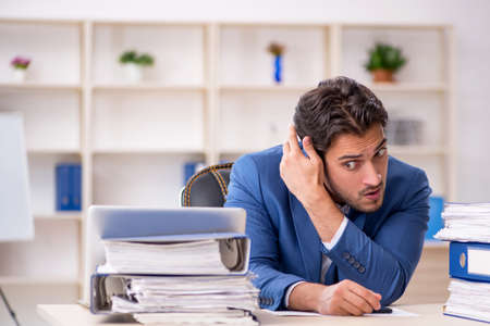Young male employee and too much work in the officeの写真素材