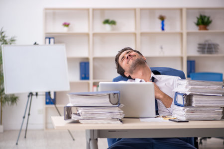 Young male employee and too much work in the officeの写真素材