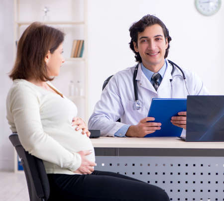 Old pregnant woman visiting young male doctorの写真素材