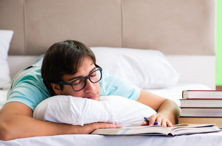 Student preparing for exams at home in bedroom lying on the bedの写真素材