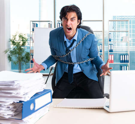Chained male employee unhappy with excessive workの写真素材