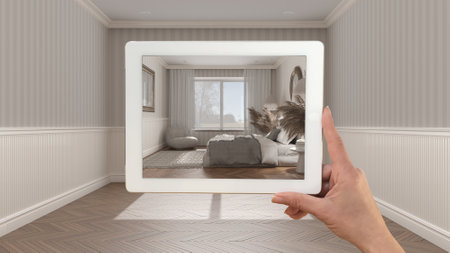 Augmented reality concept. Hand holding tablet with AR application used to simulate furniture and design products in empty interior with parquet floor, classic bedroom with decorsの写真素材