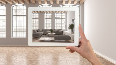 Augmented reality concept. Hand holding tablet with AR application used to simulate furniture and design products in empty interior with parquet floor, modern living room with sofaの写真素材