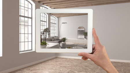 Augmented reality concept. Hand holding tablet with AR application used to simulate furniture and design products in empty interior with parquet floor, living dining room and kitchenの写真素材