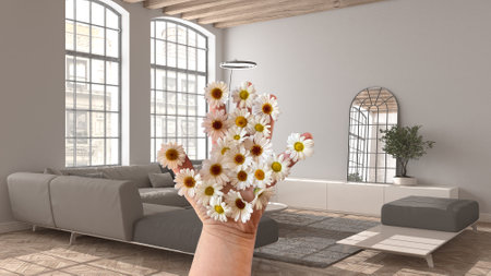 Woman's hand holding daisies, spring and flowers idea, over modern living room with sofa and big windows, wooden roof beams, lamp, parquet floor, interior design ideaの写真素材