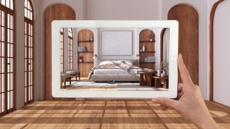 Augmented reality concept. Hand holding tablet with AR application used to simulate furniture and design products in empty interior with parquet floor, japandi bedroomの写真素材