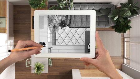 Hands holding and drawing on tablet showing kitchen, living and dining room details CAD sketch. Real...