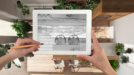 Hands holding and drawing on tablet showing kitchen and dining room details CAD sketch. Real finished interior in the background, architecture design presentationの写真素材