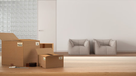 Wooden table, desk or shelf with stack of cardboard boxes over blurred view of sitting waiting room with glass brick wall, interior design, moving house concept with copy spaceの写真素材
