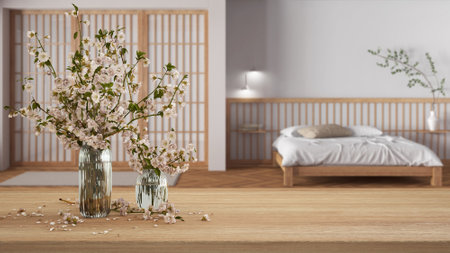 Wooden table, desk or shelf close up with branches of cherry blossoms in glass vase over blurred view of japandi bedroom, minimalist interior design conceptの写真素材