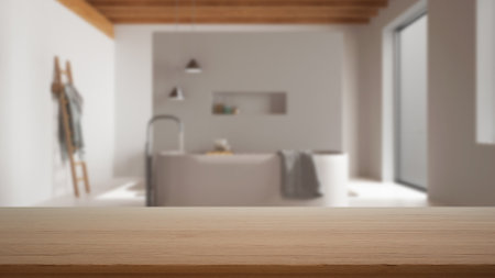 Empty wooden table, desk or shelf with blurred view of minimal white bathroom with bathtub, resin floor and wooden ceiling, modern interior design conceptの写真素材