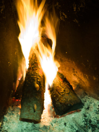 Fireplace with burning wood logs and bright orange yellow flames, radiating cozy warmth and glowing...