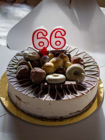 Round chocolate decorated birthday cake with numbered candles 66, creamy frosting and festive decorations celebrating a joyful milestone, perfect for parties and anniversariesの写真素材