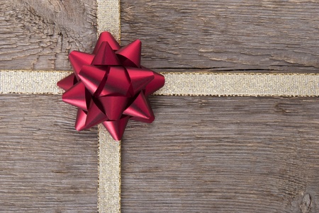 a red bow on a golden ribbon on wood as backgrounの写真素材