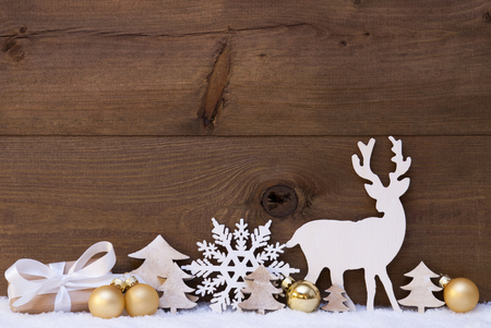 Christmas Card With Golden Festive Decoration On Snow. Gift, Present, White Reindeer, Christmas Ball, Christmas Tree,, Snowflake. Brown, Rustic, Vintage Wooden Background. Copy Space For Advertisementの写真素材