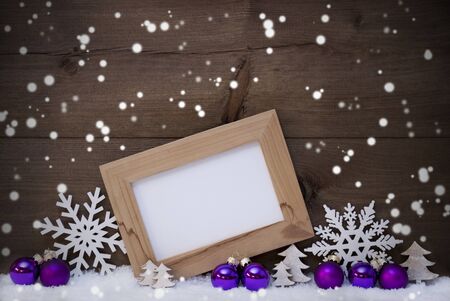 Brown Christmas Card With Purple Christmas Decoration On White Snow, Snowflakes. Picture Frame With Copy Space For Advertisement, Star, Heart And Christmas Tree Ball. Rustic, Vintage Wooden Backgroundの写真素材