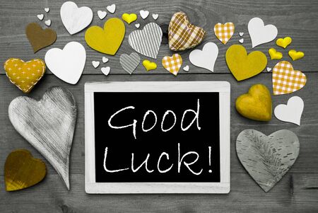Chalkboard With English Text Good Luck. Many Yellow Textile Hearts. Wooden Background With Vintage, Rustic Or Retro Style. Black And White Image With Colored Hot Spots.の写真素材