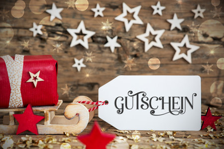 Sled With Gift, Christmas Bokeh Background With German Text Gutscheinの写真素材