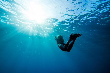 girl swimming underwater in deep blue tropical seaの写真素材