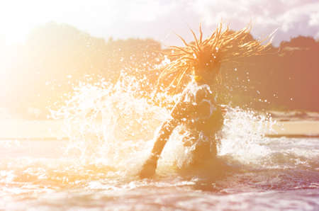 girl jumping in the water with splash and sun flare. summer beach colorful backgroundの写真素材