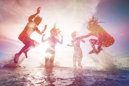 Silhouettes of happy young people jumping in sea at the beach on summer sunsetの写真素材