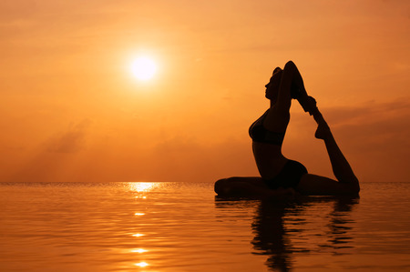 Silhouette young woman practicing yoga on the beach at sunsetの写真素材