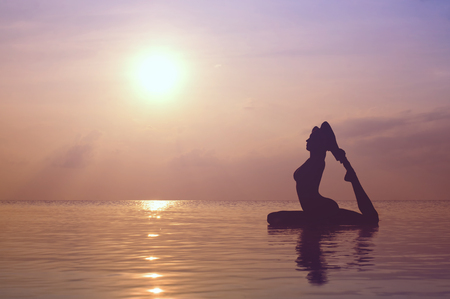 Silhouette young woman practicing yoga on the beach at sunsetの写真素材