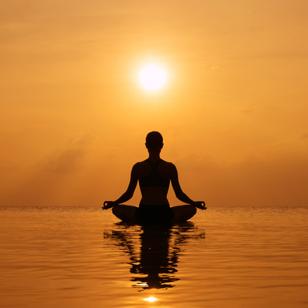Silhouette young woman practicing yoga on the beach at sunsetの写真素材