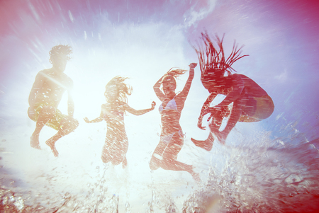 summer silhouettes of happy young people jumping in sea on the beach. vintage retro style with soft focus and sun flareの写真素材
