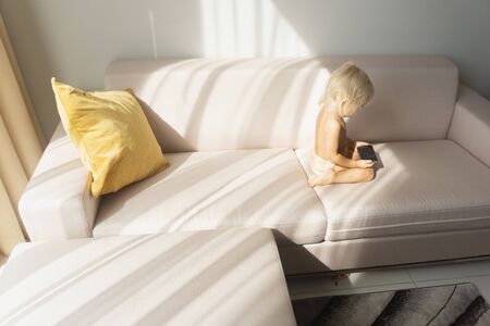child sits on the couch and looks at the smartphoneの写真素材