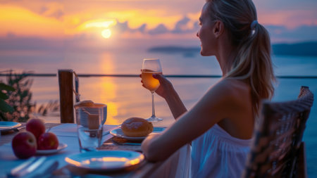 A romantic woman sitting at table with a glass of wine and a plate of food on terrace on vacationの素材